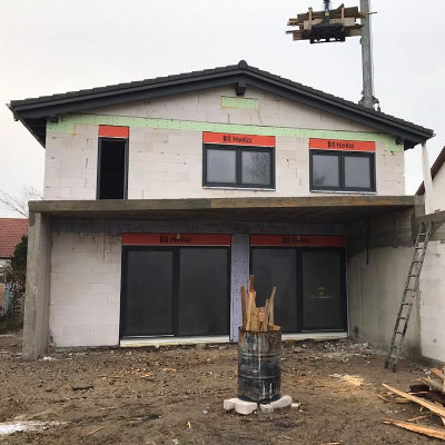 Ein zweistöckiges Haus im Bau mit weißen Wänden, Fenstern und einer Baustelle im Vordergrund.